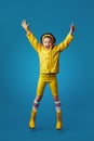 Full body excited kid girl in yellow raincoat and boots smiling and jumping