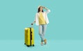 Happy woman in casual summer clothes standing with yellow travel bag on turquoise background Royalty Free Stock Photo