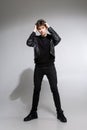 Full body image of model appearance of young fashionable guy in leather jacket and all black clothes posing on white