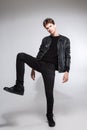 Full body image of model appearance of young fashionable guy in leather jacket and all black clothes posing on white