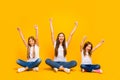 Full body photo of amazing three ladies sitting floor raising fists up wear casual clothes isolated yellow background