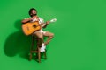 Full body photo of attractive young man sit chair sing play guitar wear trendy citrus print clothes isolated on green Royalty Free Stock Photo