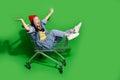 Full body photo of attractive young woman shopping cart have fun excited wear trendy jeans clothes isolated on green Royalty Free Stock Photo