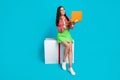 Full body photo of attractive young woman sit cube orange netbook eshop dressed stylish green skirt isolated on