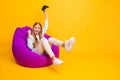 Full body photo of beautiful little lady good mood playing video games joystick sitting cozy violet bean bag rejoicing Royalty Free Stock Photo