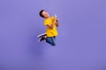 Full body photo of charming young boy hold device ball jumping playful wear yellow outfit isolated on purple color