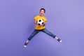 Full body photo of charming young boy hold soccer ball jumping playful wear yellow outfit isolated on purple color