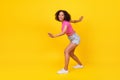 Full body photo of cheerful pretty girl have fun sneaky walk toothy smile isolated on yellow color background