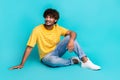 Full body photo of cheerful young man sitting floor look empty space ad isolated on teal color background Royalty Free Stock Photo