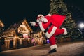 Full body photo of excited funky aged santa claus hold presents bag raise fist running garland decoration city center Royalty Free Stock Photo