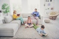 Full body photo of focused mom dad sit couch two little kids on floor read paper book in house indoors Royalty Free Stock Photo