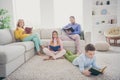 Full body photo of focused mom dad sit couch two small kids boy girl lying floor read book in house indoors Royalty Free Stock Photo