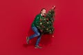Full body photo of funky man arms hold pine fir tree sneaky walking isolated on red color background
