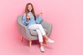 Full body photo of funky teenager schoolkid girl sit sofa relax smartphone finger direct copyspace follow media isolated