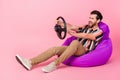 Full body photo of funny aggressive young man lying beanbag with steering wheel beep when see another car isolated on
