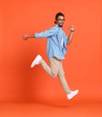 Full body photo of happy crazy african american guy jumping isolated over orange background