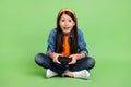 Full body photo of impressed little girl play station wear shirt jeans hairband sneakers isolated on green background Royalty Free Stock Photo