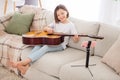 Full body photo of young cheerful girl happy positive smile online lesson learn play guitar sit sofa home Royalty Free Stock Photo
