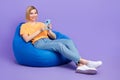 Full body photo of young girl browsing smartphone relaxed chilling bean bag pouf comfortable dorm room isolated on