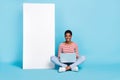 Full body photo of young girl guy sit floor use laptop manager promoter board isolated over blue color background Royalty Free Stock Photo