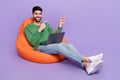 Full body photo of young latin arab man sit beanbag laptop point empty space wear stylish green look on purple