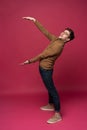 Full body picture of a young casual man presenting something on pink background. Royalty Free Stock Photo