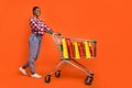 Full body portrait of cheerful nice lady push trolley look empty space isolated on orange color background