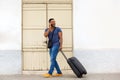 Full body handsome young guy walking with suitcase and talking on mobile phone Royalty Free Stock Photo