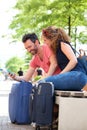 Happy couple sitting outside in park with suitcase and cellphone Royalty Free Stock Photo
