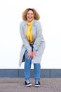 Full body happy young african american woman in winter coat laughing by white wall