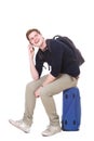 Full body happy young man sitting on suitcase and talking on mobile phone Royalty Free Stock Photo