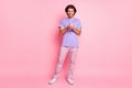 Full body portrait of satisfied guy typing sms look phone purple clothing isolated on pink color background