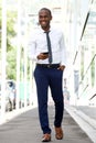 Full body smiling african american businessman walking on city street with cellphone Royalty Free Stock Photo