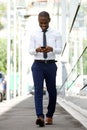 Full body smiling african american businessman walking with mobile phone on city street Royalty Free Stock Photo