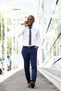 Full body smiling african american businessman walking and talking with mobile phone on city street Royalty Free Stock Photo