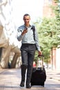 Full body traveling businessman walking in city with suitcase and mobile phone Royalty Free Stock Photo