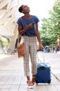 Full body young african american woman walking in city with suitcase and mobile phone Royalty Free Stock Photo