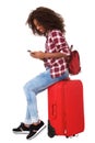 Full body young african woman sitting on suitcase and using mobile phone over white background Royalty Free Stock Photo