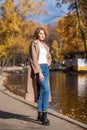 Portrait of a young beautiful blonde woman in coat and blue jeans, autumn park outdoors Royalty Free Stock Photo