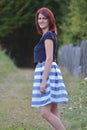 Full body portrait of young redhead woman smiling with green scenery behind