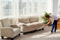 Full body portrait of young woman in white shirt and jeans cleaning carpet with vacuum cleaner in living room, copy space. Royalty Free Stock Photo