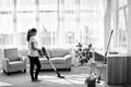 Full body portrait of young woman in white shirt and jeans cleaning carpet with vacuum cleaner in living room, copy space. Royalty Free Stock Photo
