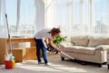 Full body portrait of young woman in white shirt and jeans cleaning carpet with vacuum cleaner in living room, copy space. Royalty Free Stock Photo