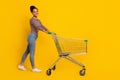 Full body profile photo of attractive positive girl walk push trolley isolated on yellow color background