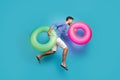 Full body profile photo of funky active guy tourist jump high rush swimming hold two colorful lifebuoys circles wear