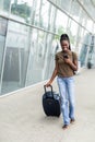 Full body profile portrait of young african woman walking with suitcase and cellphone in airport terminal Royalty Free Stock Photo