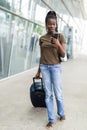 Full body profile portrait of young african woman walking with suitcase and cellphone in airport terminal Royalty Free Stock Photo