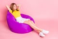 Full body profile side photo of young girl happy positive smile hands behind head comfort sit chair isolated over pastel