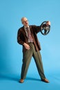 Full body shoot of young balded and mustache man holding car wheel over blue studio background. Vertical photo.