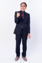 Full body shot of happy Japanese businessman in suit pointing finger Royalty Free Stock Photo